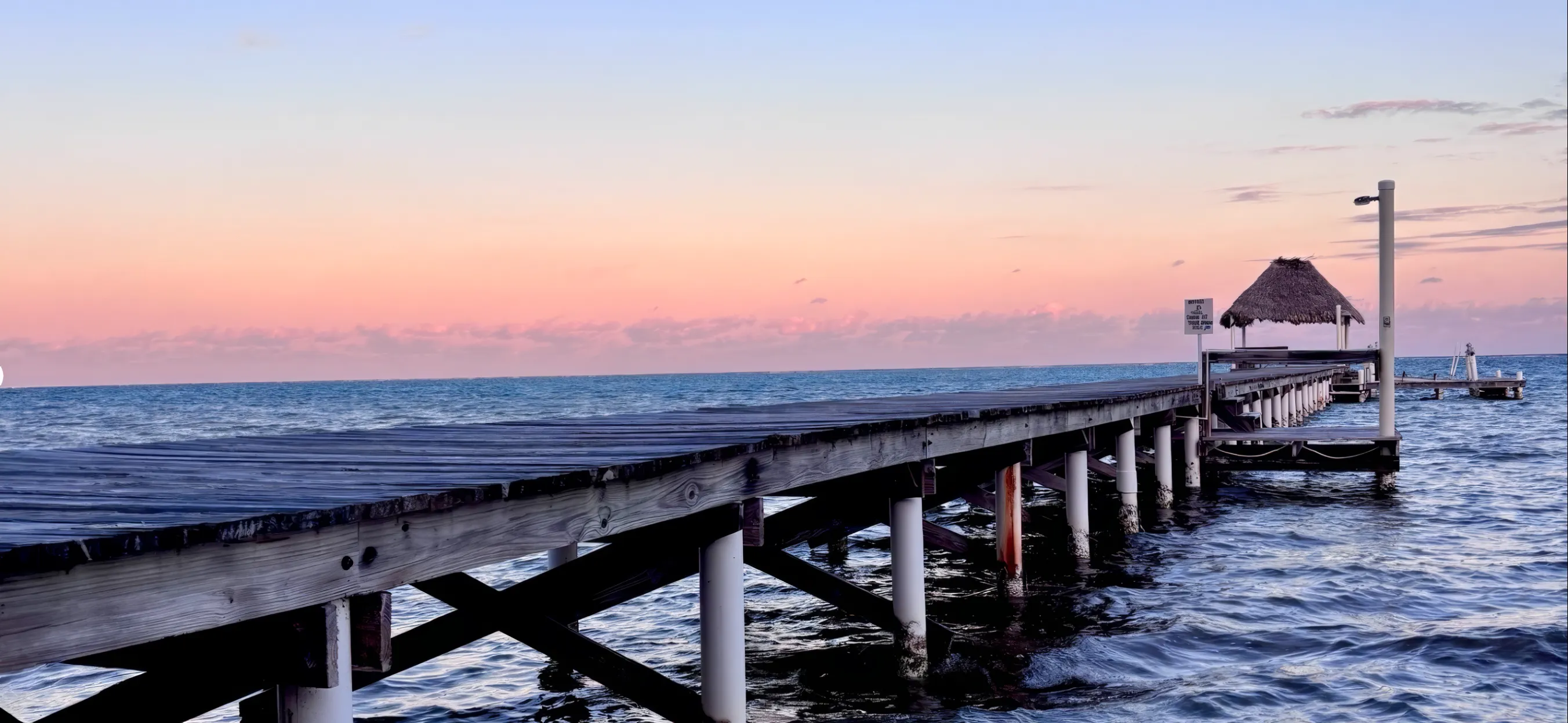 The villa's long pier and its palapa at dusk, with a pink sky over a calm sea