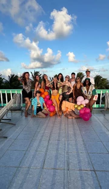 A large group of friends posing together on the rooftop deck under a blue sky