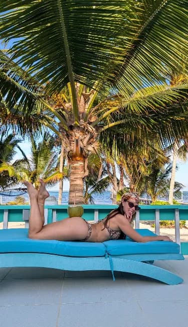 A guest relaxing on a turquoise lounger beneath a coconut palm