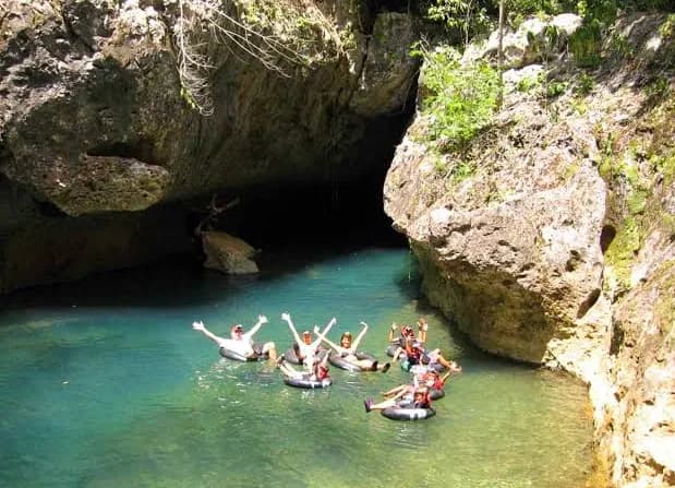 A group floating on inner tubes down a green river, at the mouth of a limestone cave