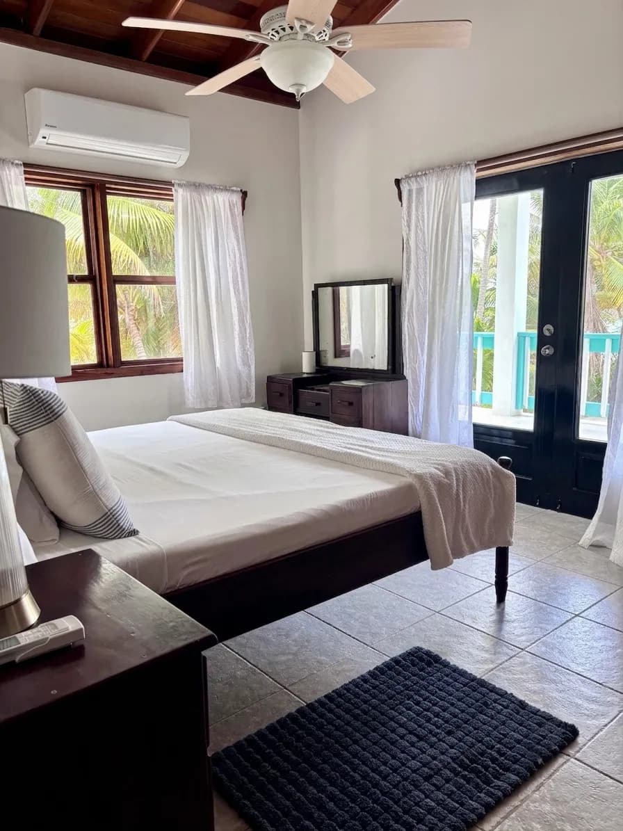 A bedroom with a ceiling fan and glass doors open to a turquoise veranda railing