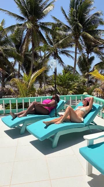 Two guests relaxing on turquoise loungers on the sunny pool deck